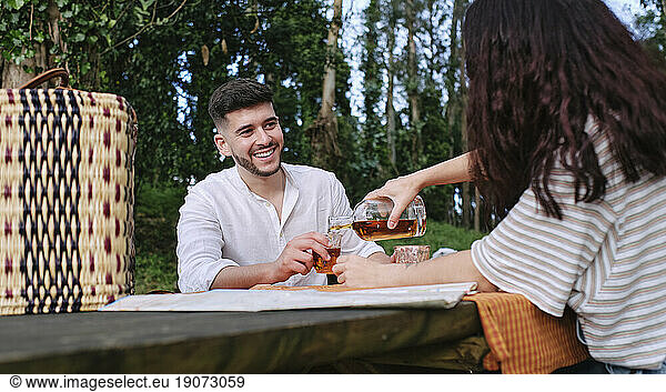 Woman serving drink to boyfriend sitting at table in forest