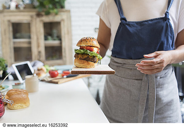Woman serving hamburger on cutting board in kitchen