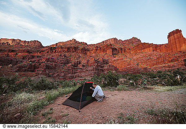 woman sets up her tent under the orange red glow of fisher towers moab