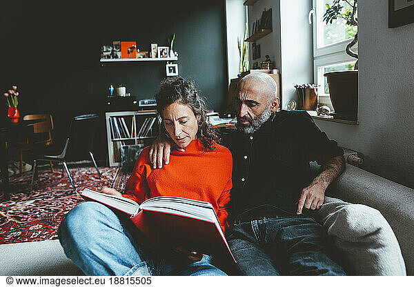 Woman sharing book with man sitting on sofa at home