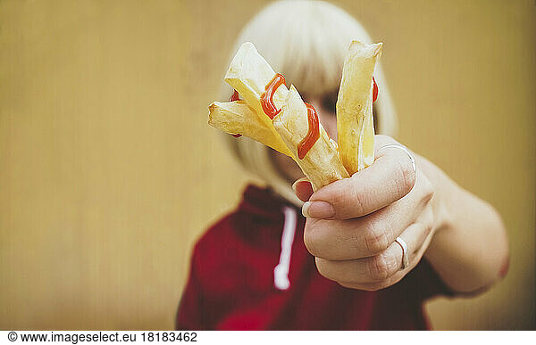 Woman showing French fries with ketchup in front of face