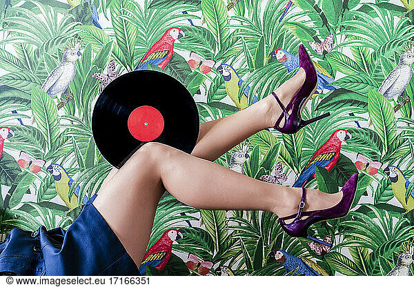 Woman showing legs and record against wallpaper in jungle and parrots pattern