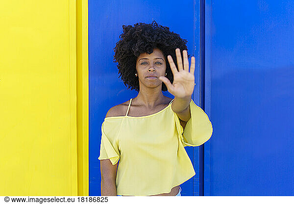 Woman showing stop gesture in front of two tone color wall