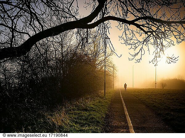 Woman silhouette walking jogging in a foggy morning sunrise in England