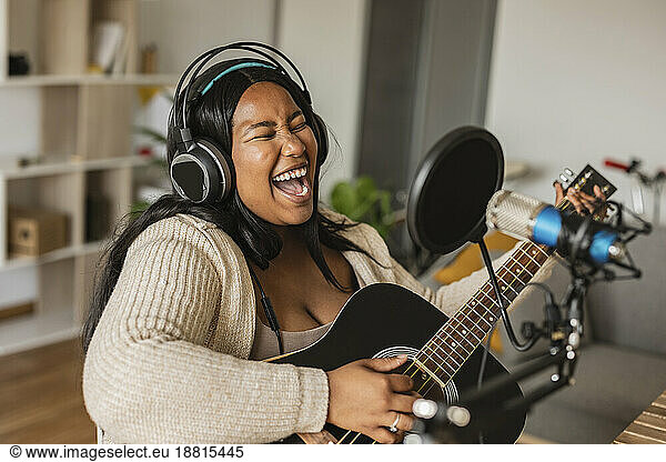 Woman singing and playing guitar on microphone at home