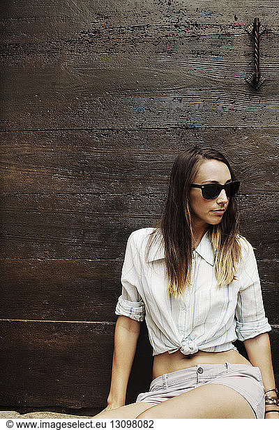 Woman sitting against wooden wall