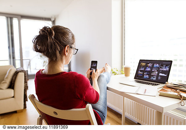 Woman sitting at desk at home using smartphone