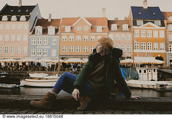 Woman sitting at harbor in front of buildings in city