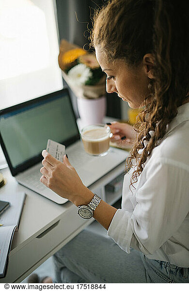 Woman sitting at her working desk and looking at her credit card