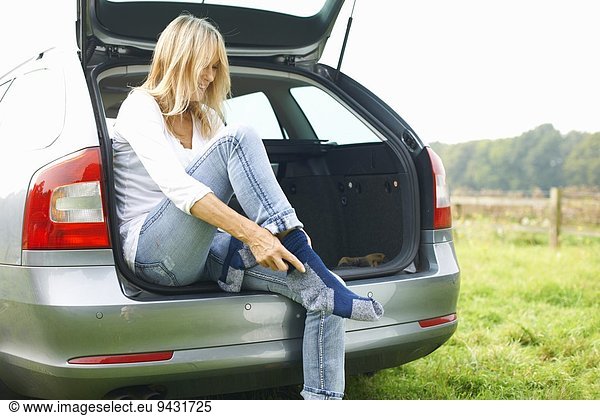 Woman sitting at rear of car putting on socks