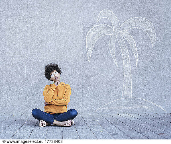 Woman sitting cross-legged on ground in front of painted palm tree