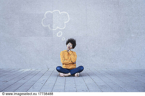 Woman sitting cross-legged on ground with empty thought bubble