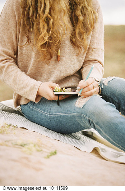 Woman sitting in a desert on a rock  holding a notebook and pencil.