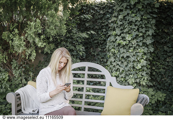 Woman sitting in a garden on a bench  using her mobile phone.