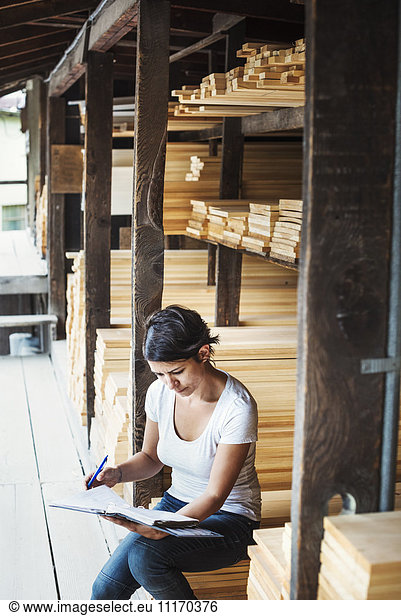 Woman sitting in a lumber yard  holding a folder.
