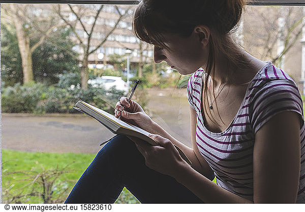 Woman sitting in front of windowpane drawing in sketchbook