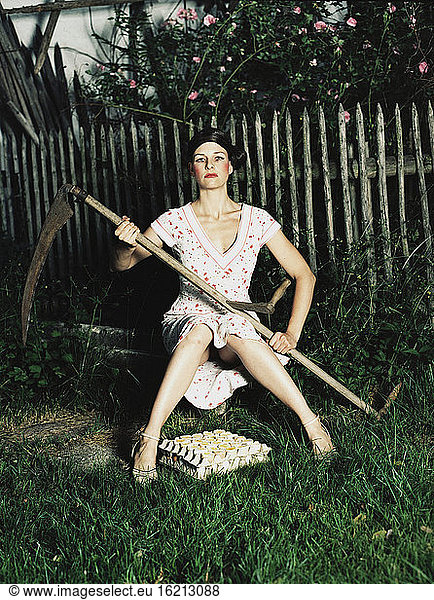 Woman sitting in garden  holding scythe
