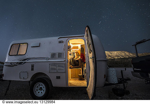 Woman sitting in illuminated camper trailer against star field