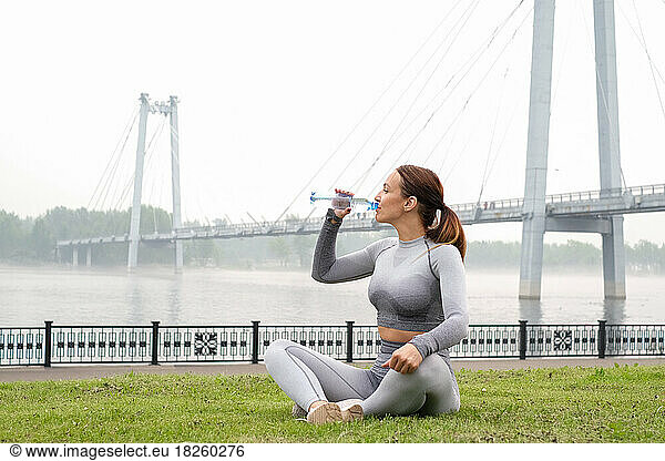Woman sitting in yoga pose   drinking water in urban background.