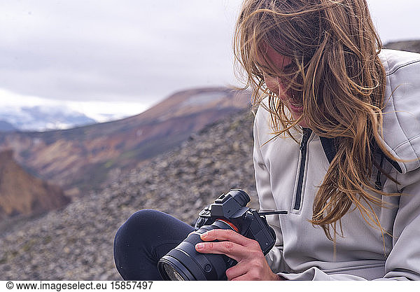 Woman sitting looking down at camera in the wind  in Landmannalaugar