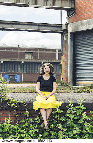 Woman sitting on a plant covered wall in an old industrial area