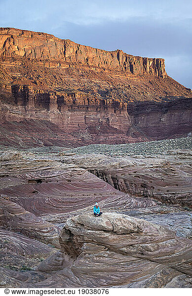 Woman sitting on a rock in a colorful desert landscape.