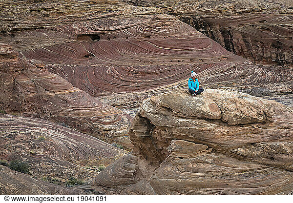 Woman sitting on a rock in a colorful desert landscape.