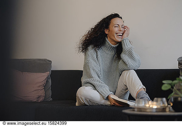 Woman sitting on couch laughing  reading a book