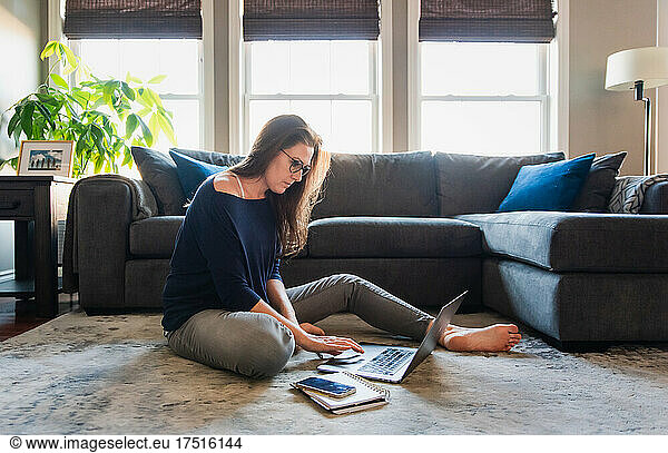 Woman sitting on floor in living room working on computer.