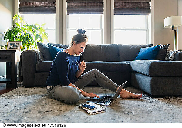 Woman sitting on floor in living room working on computer.