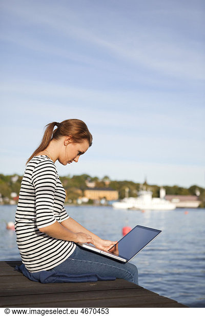 Woman sitting on jetty with computer