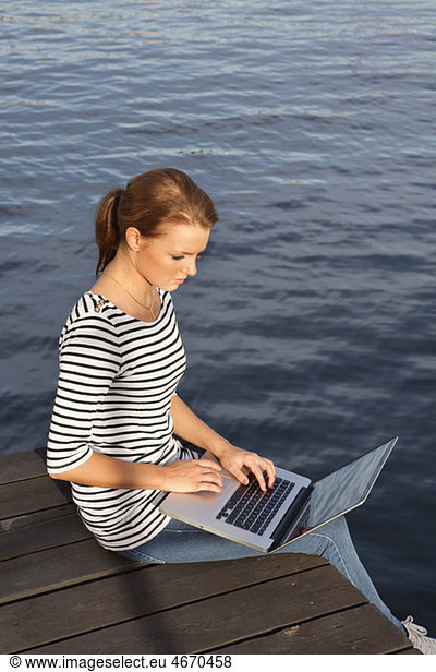 Woman sitting on jetty with computer in lap