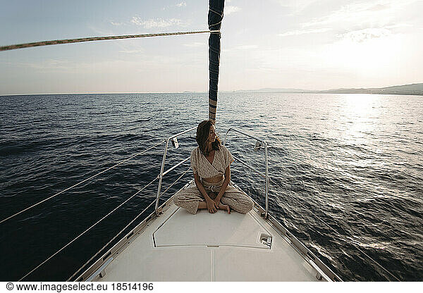 Woman sitting on sailboat and enjoying vacation at sunset