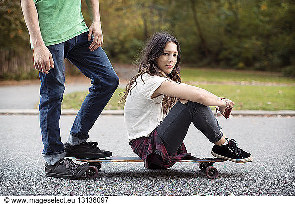 Woman sitting on skateboard with man at street