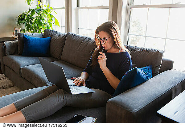 Woman sitting on sofa in living room working on computer.