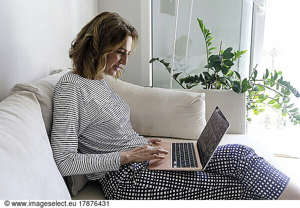Woman sitting on sofa using laptop in living room at home