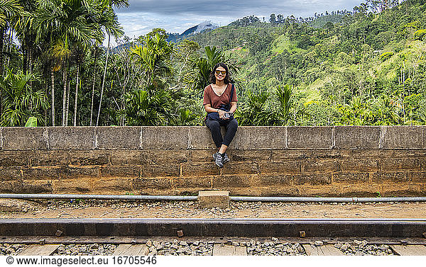 Woman sitting on stonewall at famous railroad bridge in Ella