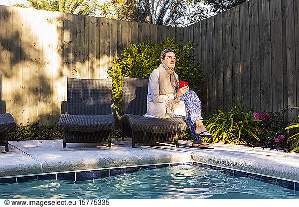 Woman sitting on sun lounger by a swimming pool