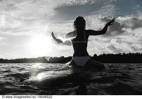 Woman sitting on surfboard in sea against sky