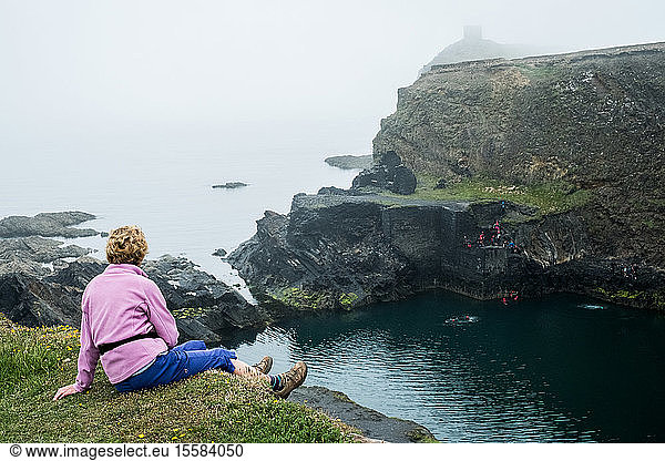 Woman sitting on top of a cliff on the Pembrokeshire Coast  Wales  UK.