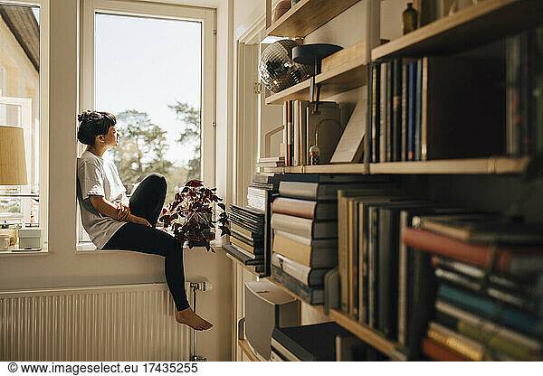 Woman sitting on window seat in sunlight at home