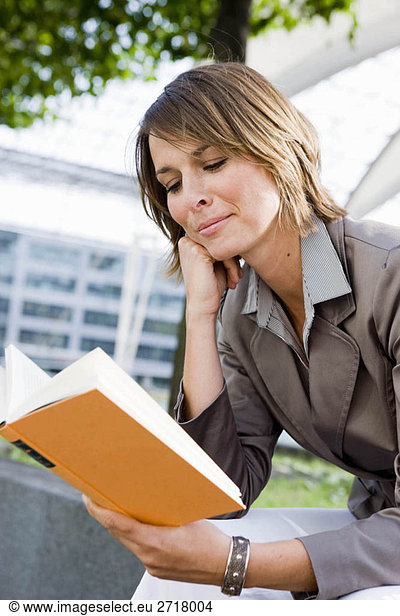 Woman sitting outdoors reading book