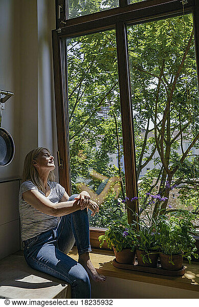 Woman sitting with eyes closed near window at home