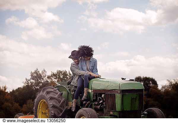 Woman sitting with man driving tractor against cloudy sky