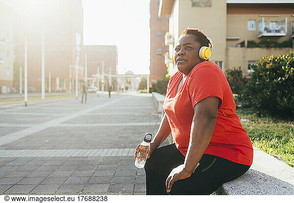 Woman sitting with water bottle listening music through wireless headphones