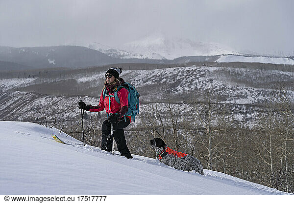 Woman ski touring with dog on snow covered mountain during vacation