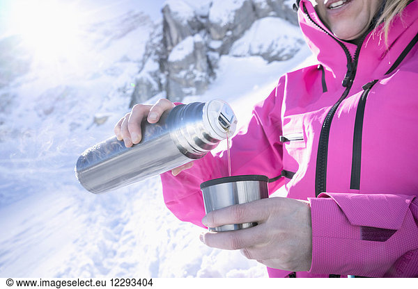 Woman skier pouring hot tea from drinks flask