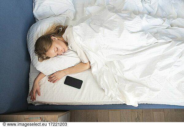 Woman sleeping by mobile phone in bed at home