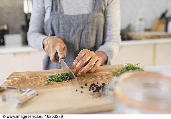 Woman slicing fresh herbs on cutting board in kitchen