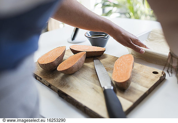 Woman slicing sweet potatoes on cutting board in kitchen